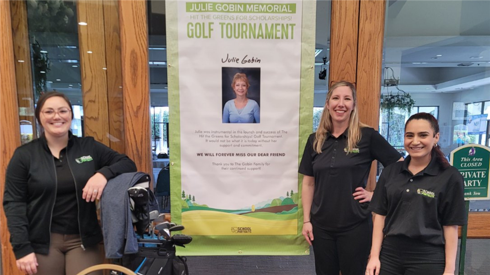   Three smiling tournament organizers standing in front of a Julie Gobin Memorial Golf Tournament ba