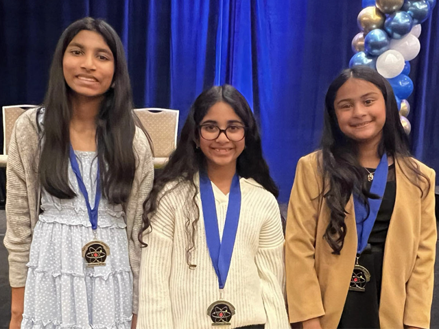 A team of three female students wearing medals at the science fair