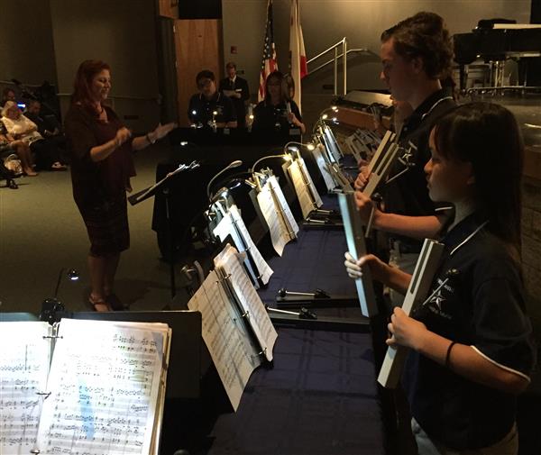 Junior high students playing chimes while being directed by an adult female teacher
